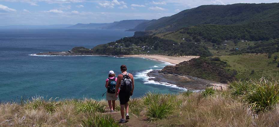 Two walkers on Royal National Park Coastal Walk atop a headland with Era Beach below them.