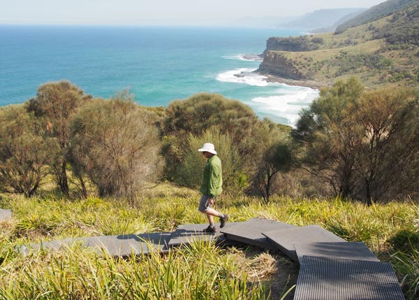 Ian from Sydney Coast Walks is walking along the boardwalk to Figure Eight Pools. Burning Palms Beach and the coastline are in the background.