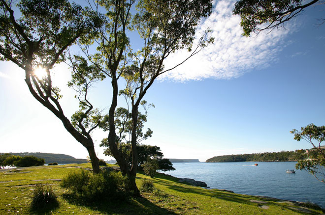 Looking from a grassy, harbourside park at Middle Head towards Sydney Heads heads in the distance. A couple of boats bob in the water on a glorious Sydney day.