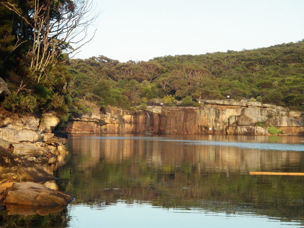 Wattamolla Lagoon on The Coast Track in Royal National Park. The water in the lagoon is unbroken except under the waterfall in the distance.